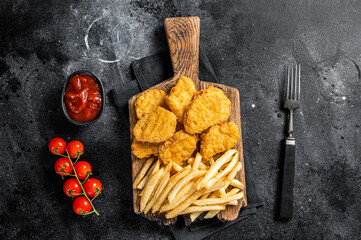 Chicken nuggets with ketchup and French fries on wooden board. Black background. Top view