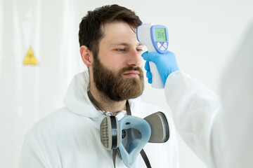 Doctor measures the temperature with an infrared thermometer to his colleague of infectious diseases. Portrait of a man doctor scientist in a lab coat. Concept of coronavirus.