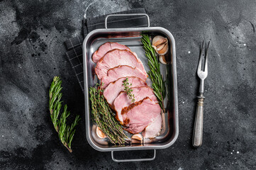 Homemade Smoked pork ham meat in steel trey with thyme and rosemary. Black background. Top view - obrazy, fototapety, plakaty