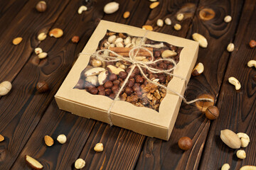 Nuts of different varieties in a box on a structural wooden background top view. Assorted nuts in a paper box..