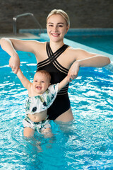 Young mother, swimming instructor and happy little girl in the pool. Teaches infant child to swim.