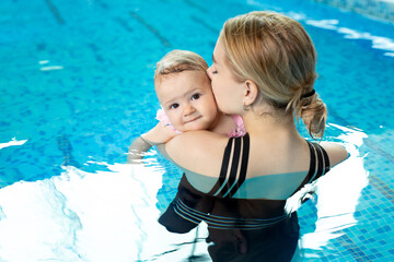 Fototapeta na wymiar A young mother holds her little daughter in the pool, hugs her and kisses her.