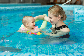 Young mother, swimming instructor and happy little girl in the pool. Teaches infant child to swim.