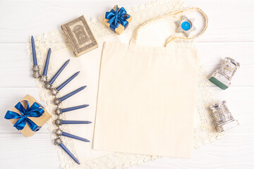 Holiday flat lay with traditional Jewish festive items and blank paper ecobag on white wooden table upper view. Old rituals