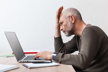 Upset elderly man looking at laptop while working - Powered by Adobe