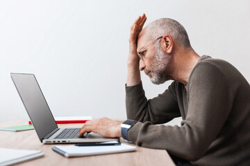 Upset elderly man looking at laptop while working