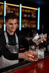 Barman puts the ice cubes into a glass with alcoholic drink