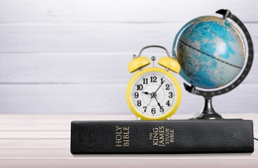 Retro alarm clock on the old holy bible with blurred world globe