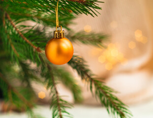 A bright golden ball hangs on a Christmas tree on a blurred shiny background. Christmas decor.