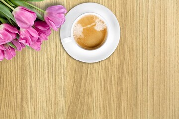 A cup of hot, morning coffee and a bouquet of tulips on a desk.