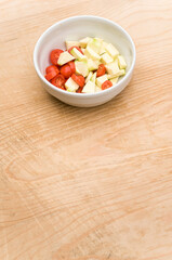 fresh zucchini and datterini tomatoes chunks in a white bowl on a rustic wooden tabletop
