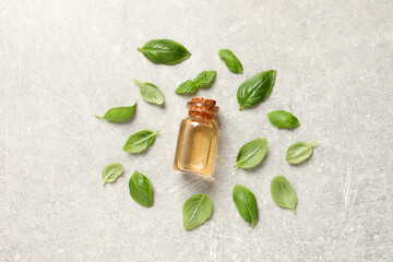 Glass bottle of basil essential oil and leaves on light grey table, flat lay