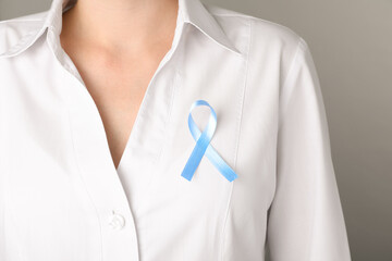 Woman with light blue awareness ribbon on grey background, closeup