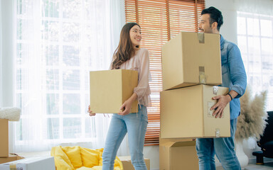 Lovely sweet Caucasian and Asian couple consist of handsome man and beautiful woman helping each other lift and carry paper boxes, moving to new comfortable house or home or apartment with happiness.