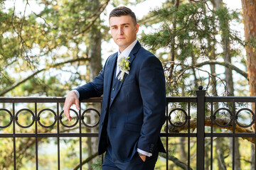 Handsome young groom wearing elegant dark blue suit looking at camera outdoors portrait. Stylish groom fashion.