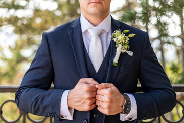 Unrecognizable young groom in elegant dark blue suit with beautiful white roses boutonniere. Groom...