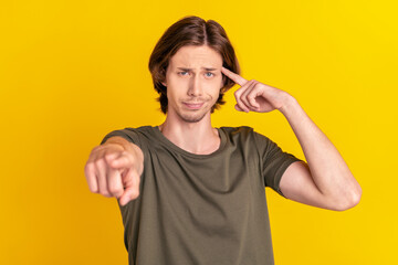 Photo of young man unhappy finger touch head accuse blame point finger you stupid isolated over yellow color background