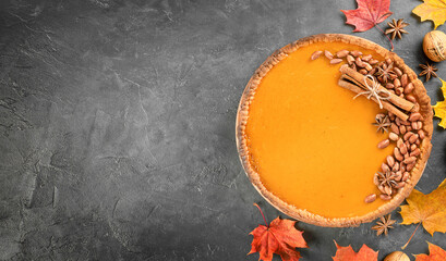 decorated pumpkin pie and autumn leaves on a dark background with copy space