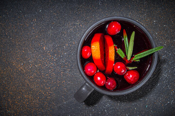 Autumn winter cranberry tea with rosemary and orange slices, dark concrete background copy space