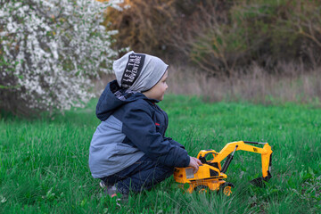Adorable little boy playing excavator in the meadow. Green grass around. Side view image