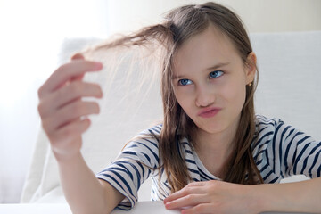 Shaggy teenage girl looking at her hair holding a lock of hair in her hands