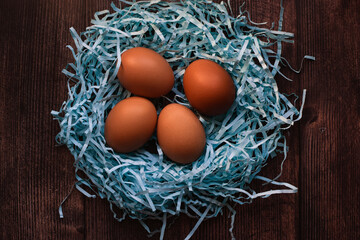 Brown chicken eggs in tender straws in the form of a bird's nest, on a wooden background. Easter holiday concept. Farm products. Top view, flat lay.