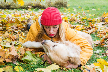 Woman in warm clothes with her retriever playing lying among autumn leaves