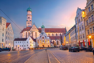 Augsburg, Germany. Cityscape image of old town street of Augsburg, Germany with the Basilica of St. Ulrich and Afra at autumn sunset. - obrazy, fototapety, plakaty