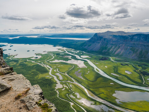 Aerial scenic view from Skierffe rock summit on glacial Rapadalen river delta valley at Sarek national park with meanders, lakes, mountains and birch trees. Summer day landscape Sweden Lapland