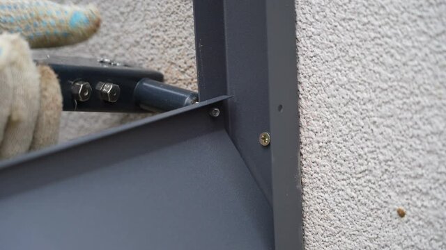Close up shot on hands of man using rivet plier to join metal profiles to the fence rails. Handyman attaching metal parts of blinds fence with tool
