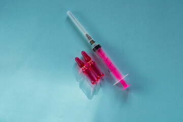 Pink medicine in ampoules (vitamin B) and a pink syringe on a blue background. Ampoules for injections. 