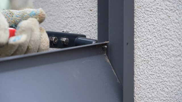 Close up shot on hands of man using rivet plier to join metal profiles to the fence rails. Handyman attaching metal parts of blinds fence with tool
