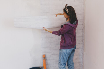 Young woman glues wallpaper at home. girl glues wallpaper in the form of a brick. repair.
