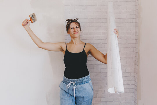 Young woman glues wallpaper at home. girl glues wallpaper in the form of a brick. repair.
