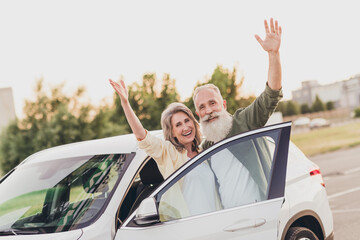 Photo of cheerful aged couple husband wife good mood waving hands hello bye ride transport car...