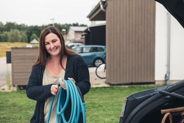 Portrait of smiling woman holding electric car charging cable at station