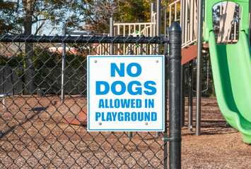 No Dogs Allowed In Playground sign on the fence of a playground