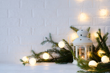 Scandinavian home decor. White lantern, fir branches and a Christmas garland.