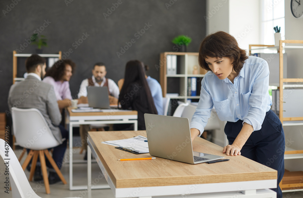 Wall mural Young caucasian woman secretary using laptop on foreground while diverse team having briefing sitting at table in conference room. Corporate office workflow, business meeting concept - Wall murals