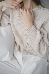 Woman hands. Woman closeup picture without face on neutral background. White interior. Very soft and nice light. Healthy and clean skin. Comfort and calm. French manicure. Good nails. Beige sweater