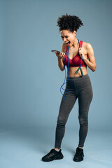 Overjoyed athlete woman is looking at the smartphone screen and rejoicing after jumping at the rope