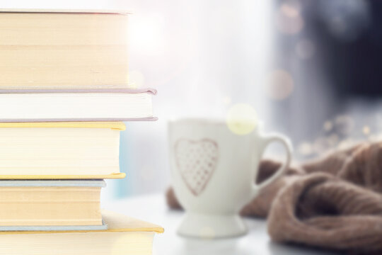 Stack of books and cup on table indoors. Bokeh effect
