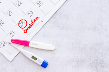Ovulation home test and thermometer on calendar with red mark