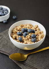 Granola with blueberry in white bowl on dark napkin.
