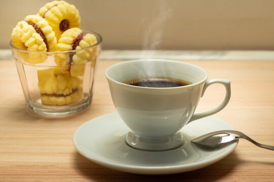 Uma x&iacute;cara com caf&eacute; quente e uma por&ccedil;&atilde;o de biscoitos amanteigados.