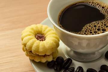 Uma xícara de café com grãos espalhados e um biscoito amanteigado.