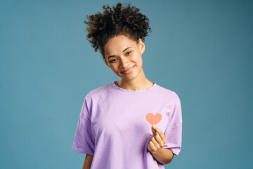 Portrait of beautiful multiracial woman with brown hair holding pink heart, symbol of breast...