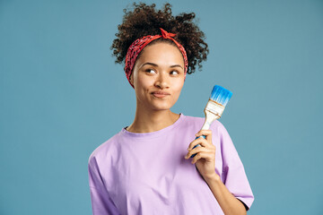 Woman holding paintbrush and looking away while pondering and preparing to the repair