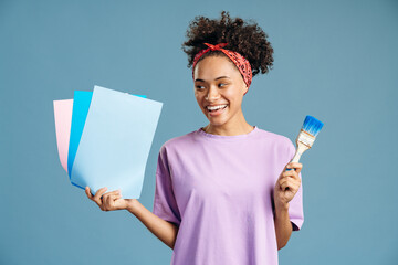 Woman looking attentively at the paper samples of colors while going to paint with brush repair equipment