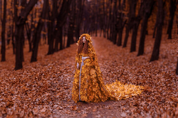 Beautiful redhead girl as a autumn in leaf cloak in forest